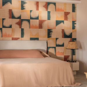 Sfeervolle slaapkamer met Elitis Tribus Comporta RM 1079 60 behang in warme aardetinten achter een bed met beige beddengoed.