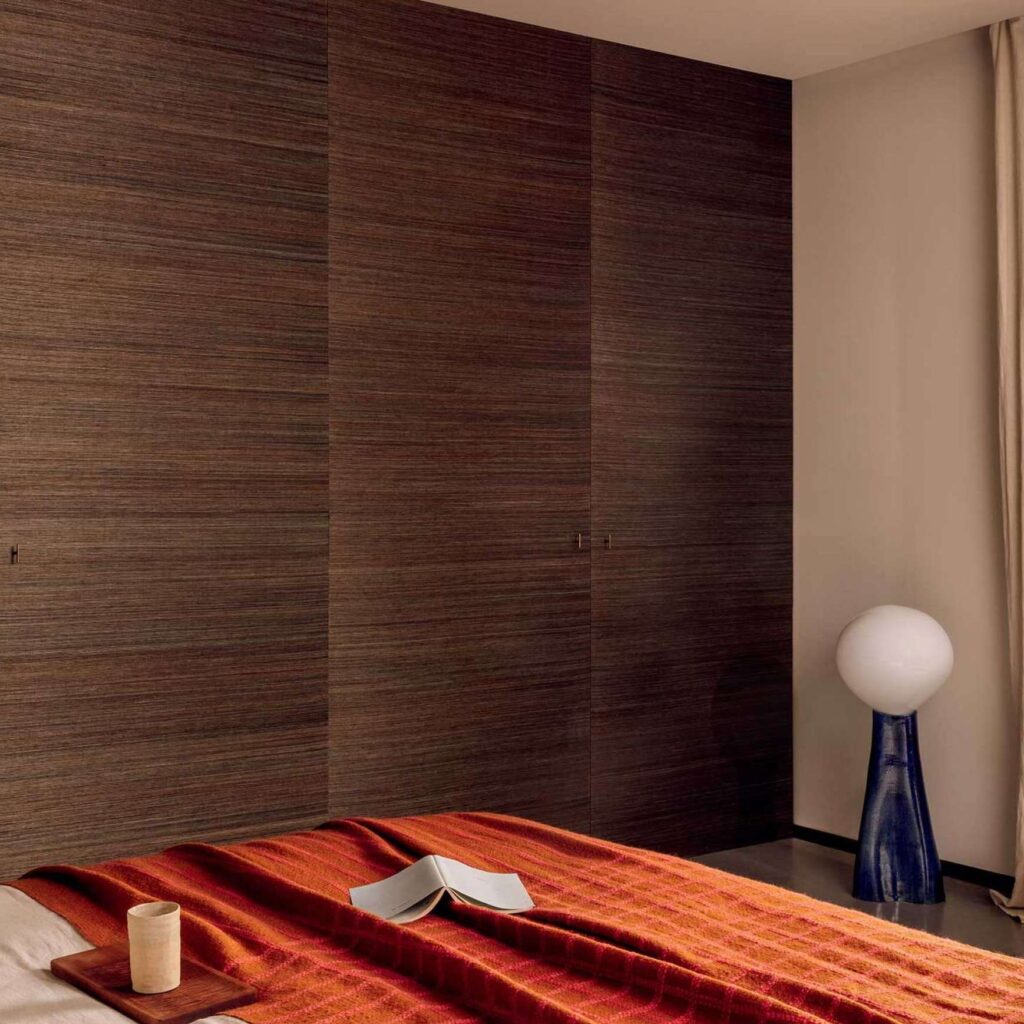 Sfeervolle slaapkamer met Elitis Tribus Favoris RM 1070 04 wandbekleding, rood dekbed en moderne verlichting.