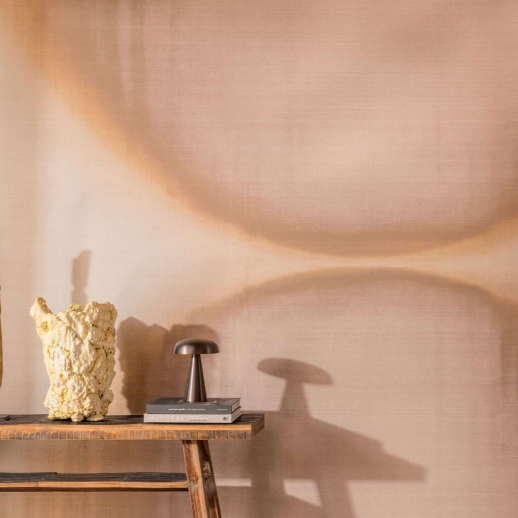 Sfeervolle interieurhoek met Elitis Tribus Itza RM 1081 04 behang, houten tafel, kunstobject en designlamp.