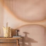 Sfeervolle interieurhoek met Elitis Tribus Itza RM 1081 04 behang, houten tafel, kunstobject en designlamp.