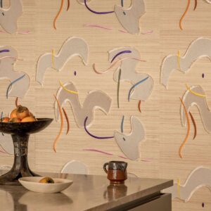 Decoratieve sfeerfoto met Elitis Tribus Lazgi RM 1100 01 behang met abstracte vormen en kleuraccenten op een beige achtergrond, met een schaal fruit en keramiek op een tafel op de voorgrond.