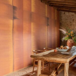 Interieur met Elitis Tribus RM 1080 35 behang in warme aardetinten, een robuuste houten eettafel en een vaas met bloemen.