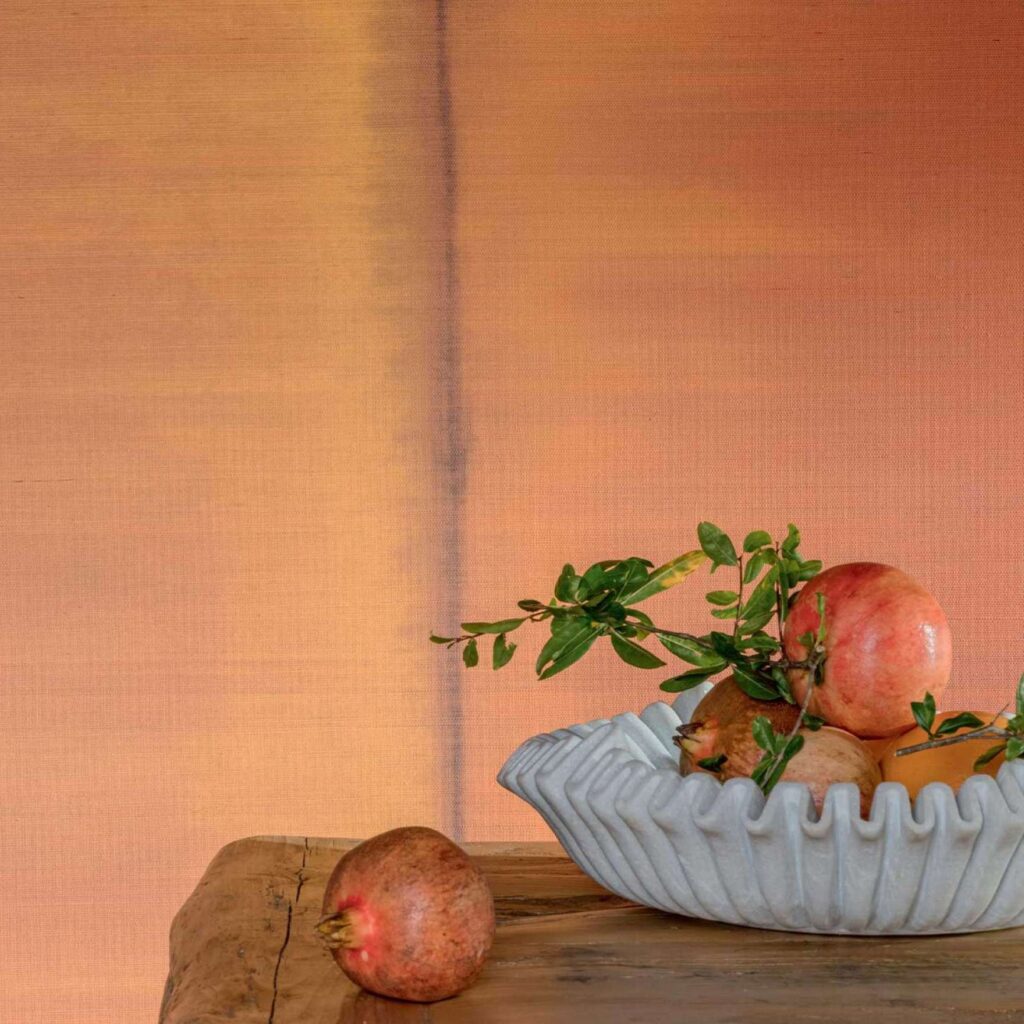 Decoratieve schaal met granaatappels op een houten tafel tegen Elitis Tribus RM 1080 35 behang in warme aardetinten.