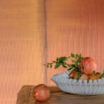 Decoratieve schaal met granaatappels op een houten tafel tegen Elitis Tribus RM 1080 35 behang in warme aardetinten.