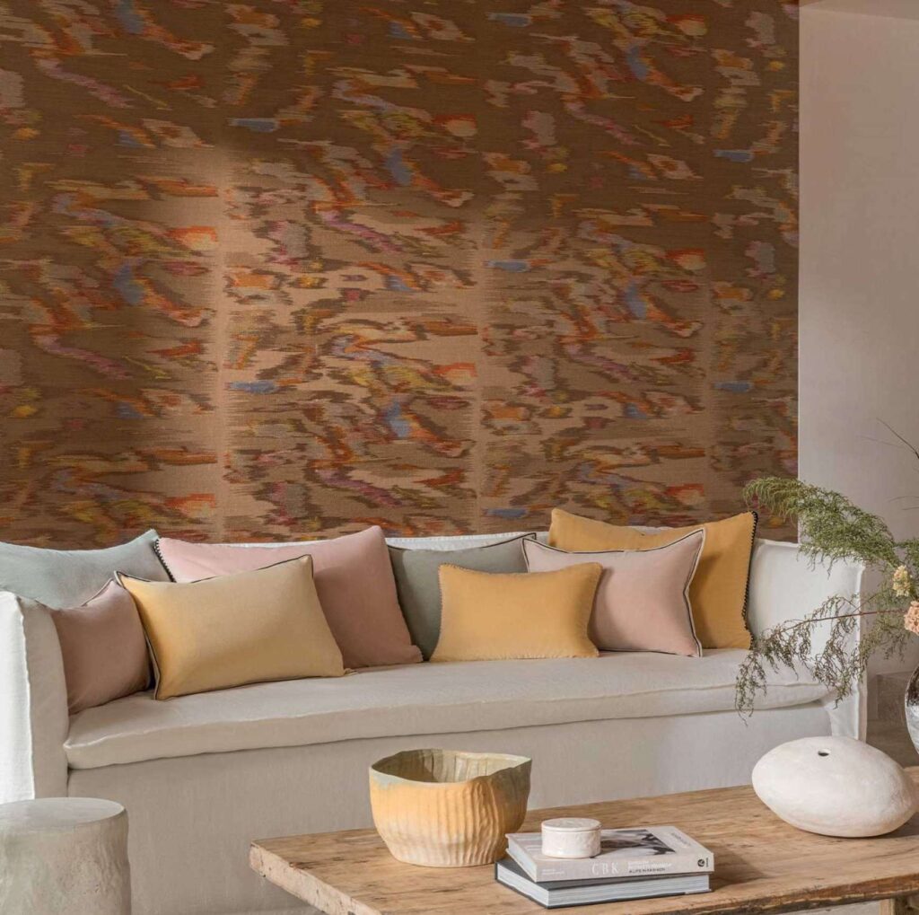 Sfeervolle woonkamer met Elitis Tribus Samarkand RM 1098 15 behang en pastelgekleurde kussens op een witte bank.