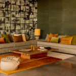 Moderne woonkamer met een Elitis vloerkleed Celeste TA 133 25 02 in warme aardetinten onder een houten salontafel en een hoekbank met gekleurde kussens.