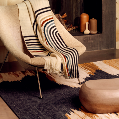 Moderne woonkamer met het Elitis-vloerkleed Emile TA 135 82 02, een designstoel met gestreepte plaid en minimalistische decoratie voor de haard.