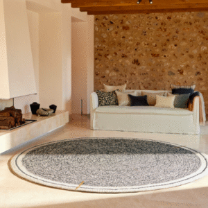 Rond Elitis vloerkleed Oscar TA 131 02 07 in een stijlvolle woonkamer met stenen muur en lichte sofa.