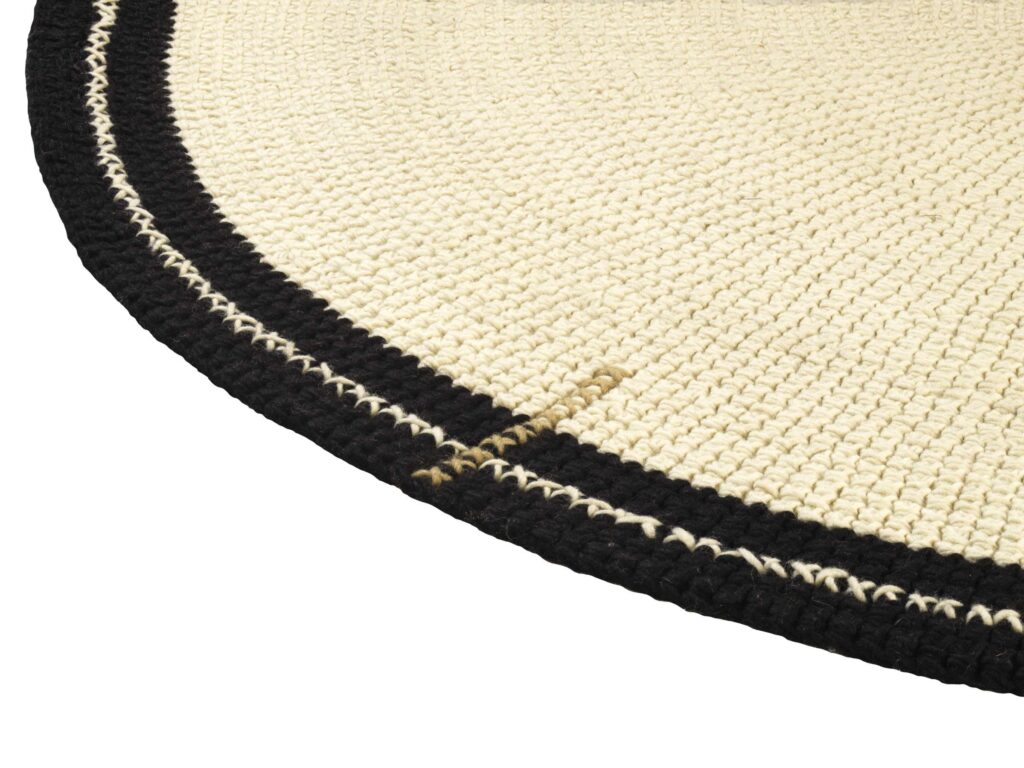 Detailopname van het Elitis vloerkleed Oscar TA 131 02 07 met een grof geweven structuur in beige en zwarte rand.