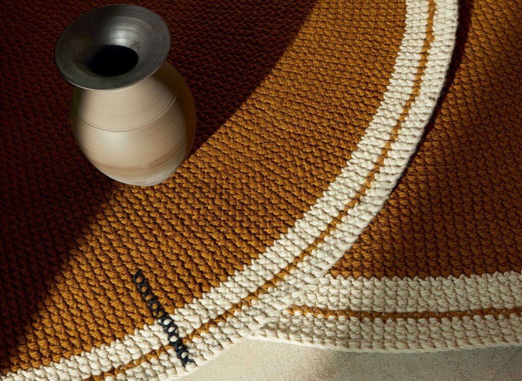 Detail van het okergele Elitis Oscar vloerkleed met witte randen en een keramische vaas erop.