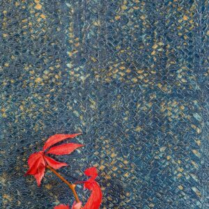 Blauw Elitis NATURAL MOOD-behang met een textuur die doet denken aan slangenleer, met een rode tak met bladeren op de voorgrond.