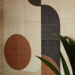 Detail van de Elitis Merida Wall Sol RM 1021-80 wandbekleding met geometrisch patroon in aardetinten en een groene plant op de voorgrond.