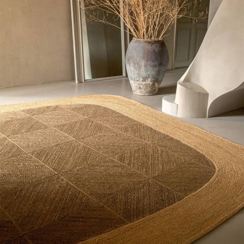 Bruin Elitiss Yasabai vloerkleed in een modern, sfeervol interieur met een grote aardewerken vaas en sculpturale trap.