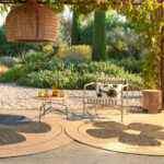 Sfeervolle buitenruimte met het Eltis Amapola vloerkleed, een tuinstoel en een hanglamp onder een houten pergola.
