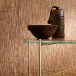 Decoratief tafereel met een rotan-achtige wandbekleding, een ronde metalen tafel en rustieke aardewerken objecten in La casa de paja op Formentera.