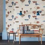 Houten bankje met kussens voor een muur met Fornasetti Macchine Volanti-behang vol fantasierijke luchtballonnen en vliegmachines.