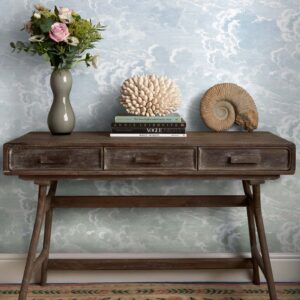 Een houten consoletafel met decoratieve objecten staat tegen Fornasetti-behang Nuvole al Tramonto met een dromerig wolkenpatroon.