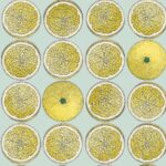 Illustratief Fornasetti-behang met een patroon van sinaasappelhelften en hele sinaasappels op een lichtblauwe achtergrond.