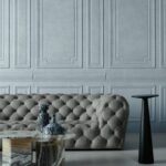 Grijze, gecapitonneerde Grandeur1-WCJ7-2-bank voor een klassieke wand met sierlijsten, met een marmeren salontafel en decoratieve vazen.