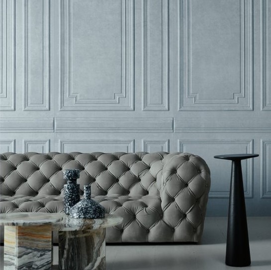 Grijze, gecapitonneerde Grandeur1-WCJ7-2-bank voor een klassieke wand met sierlijsten, met een marmeren salontafel en decoratieve vazen.