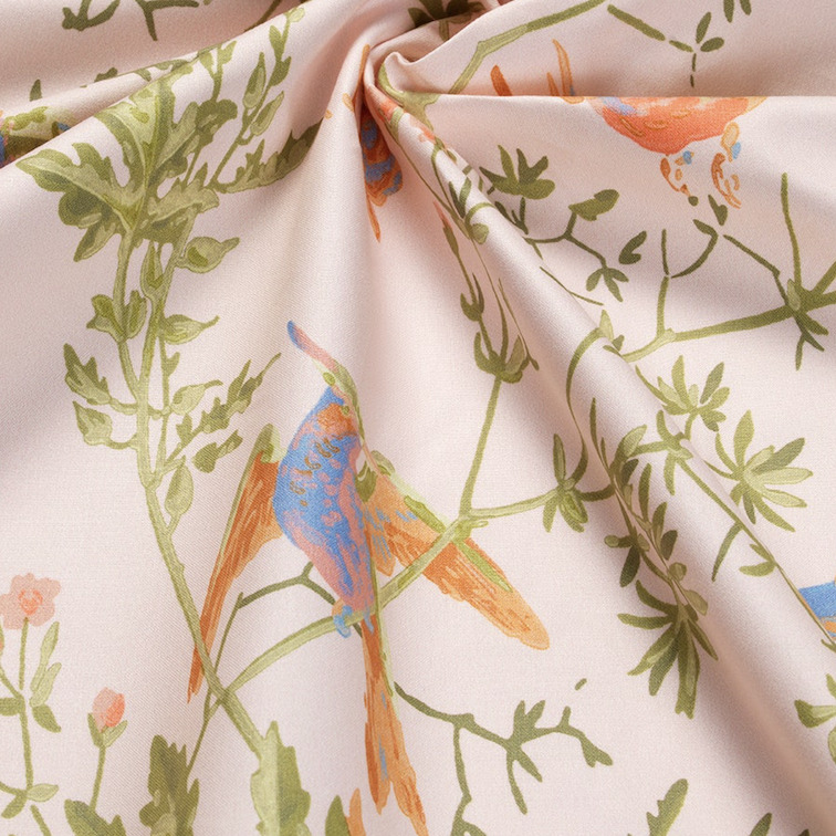 Detail van katoenen stof Hummingbirds-coton-F1253010 met kleurrijke kolibries en groene bladeren op een lichtroze achtergrond.