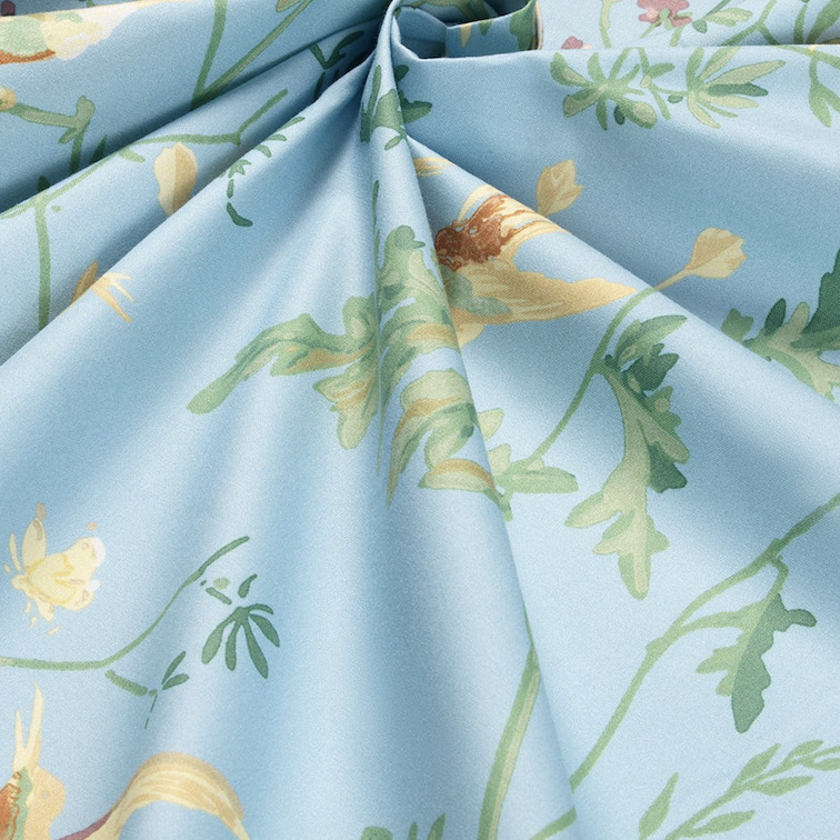 Gedetailleerde close-up van lichtblauwe katoenstof met een patroon van kolibries en bloemen.