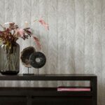 Donkere houten kast met decoratieve objecten en een vaas met droogbloemen, tegen een Itaya-Monsoon-2 behang met subtiel visgraatpatroon.
