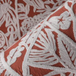 Detail van het textielontwerp 'La Perle' van LeCouturier met witte borduursels op een terracottakleurige stof.
