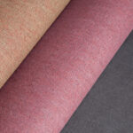 Drie opgerolde stoffen uit de LesUnis2-Q3GN collectie in beige, rood en donkergrijs met fijne textuur.