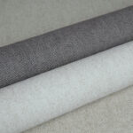 Drie opgerolde stoffen uit de LesUnis3-F4MV collectie in grijze en beige tinten met een fijne geweven structuur.