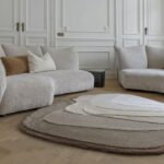 Luxe woonkamer met Limited Edition Agate High Travertine vloerkleed, omringd door zachte beige designbanken.