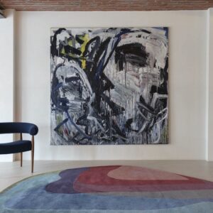 Moderne woonkamer met het Limited-Edition Agate Low Aqua Tango vloerkleed, een abstract schilderij en een donkerblauwe designstoel.