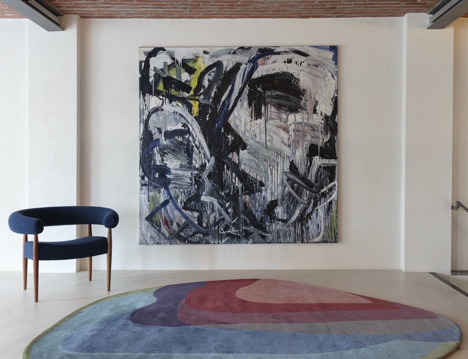 Moderne woonkamer met het Limited-Edition Agate Low Aqua Tango vloerkleed, een abstract schilderij en een donkerblauwe designstoel.