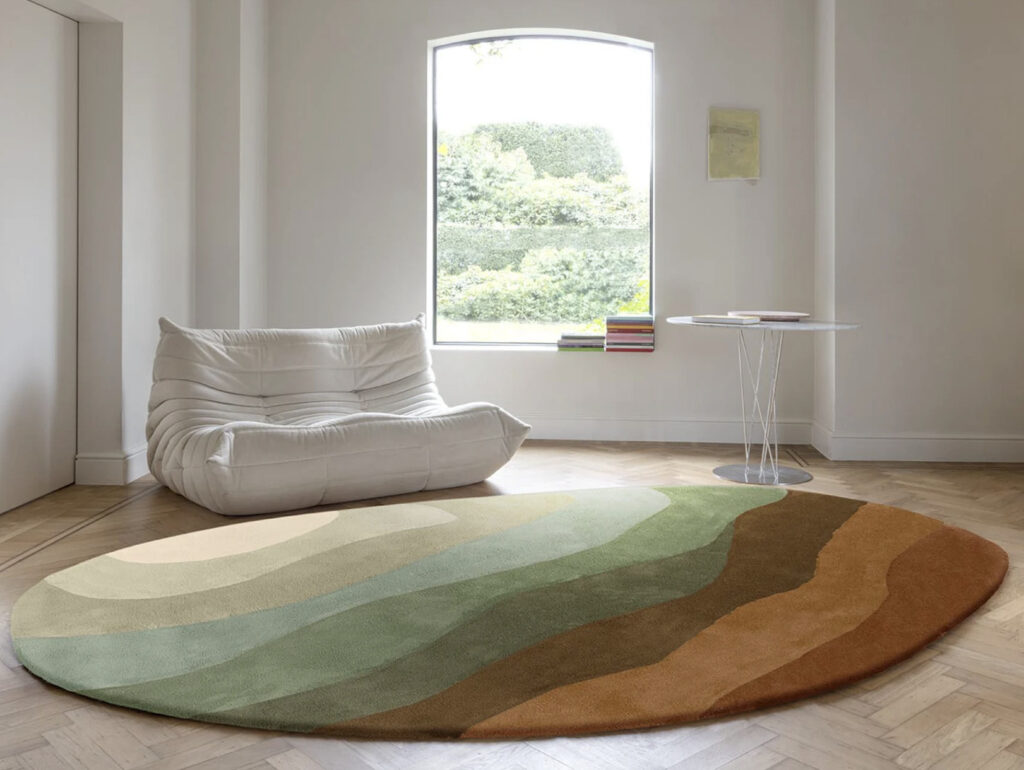 Ronde Limited Edition Allegro Low Honey Pesto vloerkleed met aardetinten in een minimalistisch interieur met een witte lounge stoel en een ronde bijzettafel.