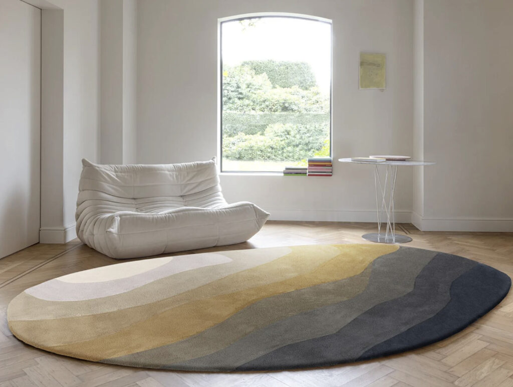Moderne woonkamer met een rond, golvend gekleurd vloerkleed Limited Edition Allegro Low Neutral Gold Organic op een houten visgraatvloer.