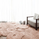 Licht ingerichte ruimte met een limited edition Atoll vloerkleed in Pale Blush en een houten loungestoel.