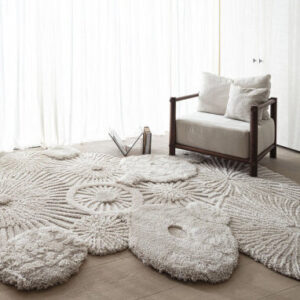 Zacht, zandkleurig Limited Edition Atoll vloerkleed met organisch patroon in een minimalistisch interieur met fauteuil.