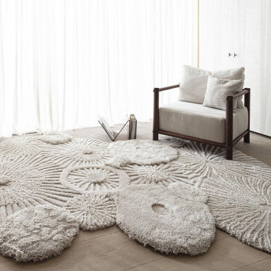 Zacht, zandkleurig Limited Edition Atoll vloerkleed met organisch patroon in een minimalistisch interieur met fauteuil.