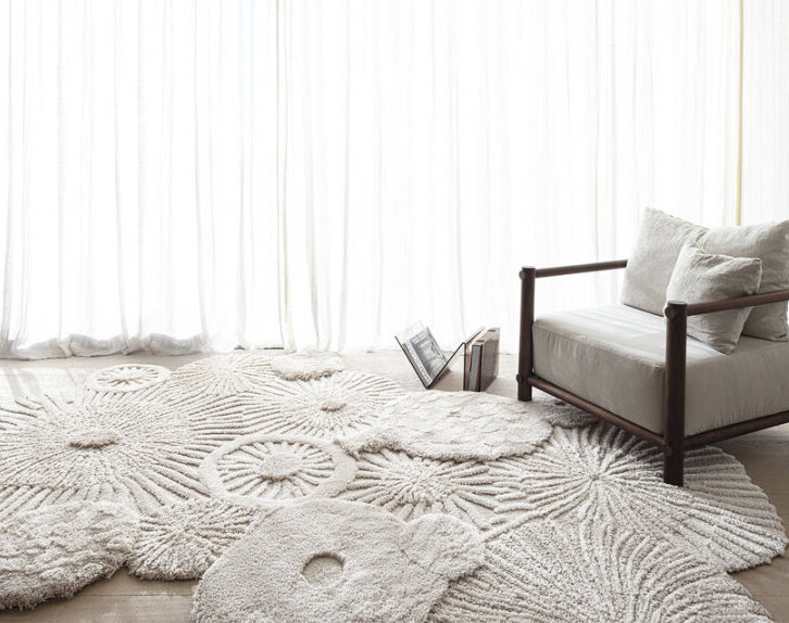 Organisch gevormd Limited Edition Atoll vloerkleed in zandkleur in een minimalistisch ingerichte kamer met een houten loungestoel.