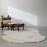 Minimalistisch interieur met een Limited-Edition vloerkleed in abstract organisch ellipsontwerp en een houten designstoel.