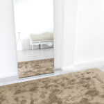 Beige Limited Edition vloerkleed Astral Cumin in moderne, minimalistische interieursetting met spiegel.