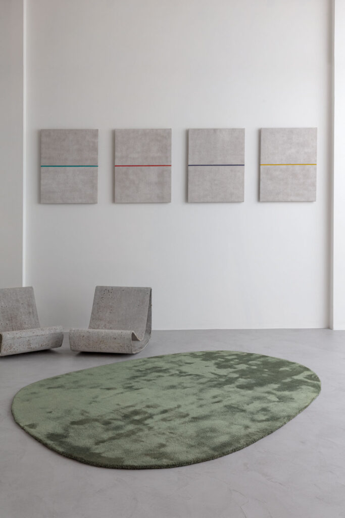 Modern interieur met het groene, organisch gevormde Limited Edition vloerkleed Astral Menthe, betonnen loungestoelen en minimalistische wandkunst.