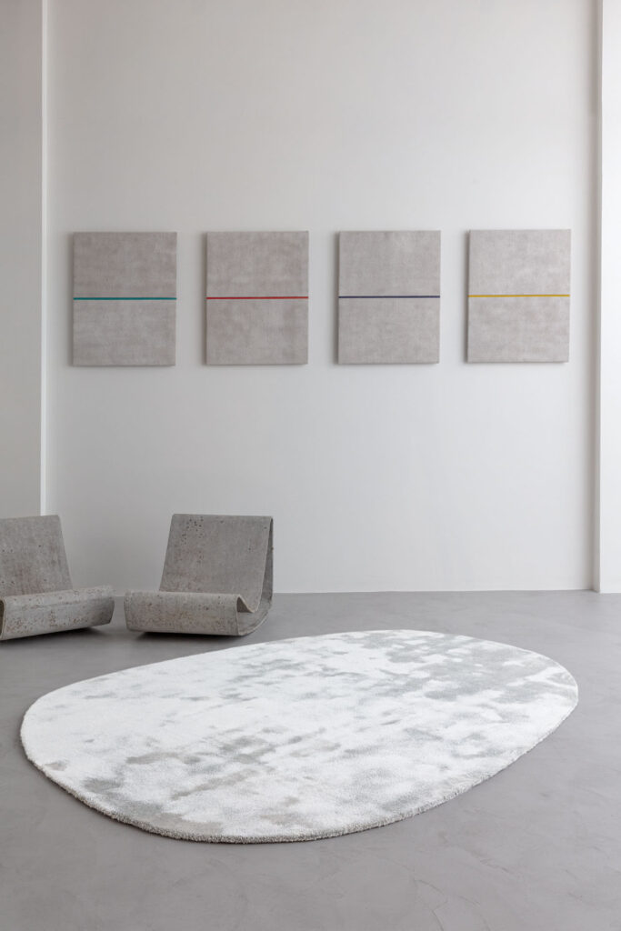 Modern interieur met het Limited Edition vloerkleed Astral White op een betonnen vloer, omringd door minimalistische stoelen en abstracte kunst aan de muur.