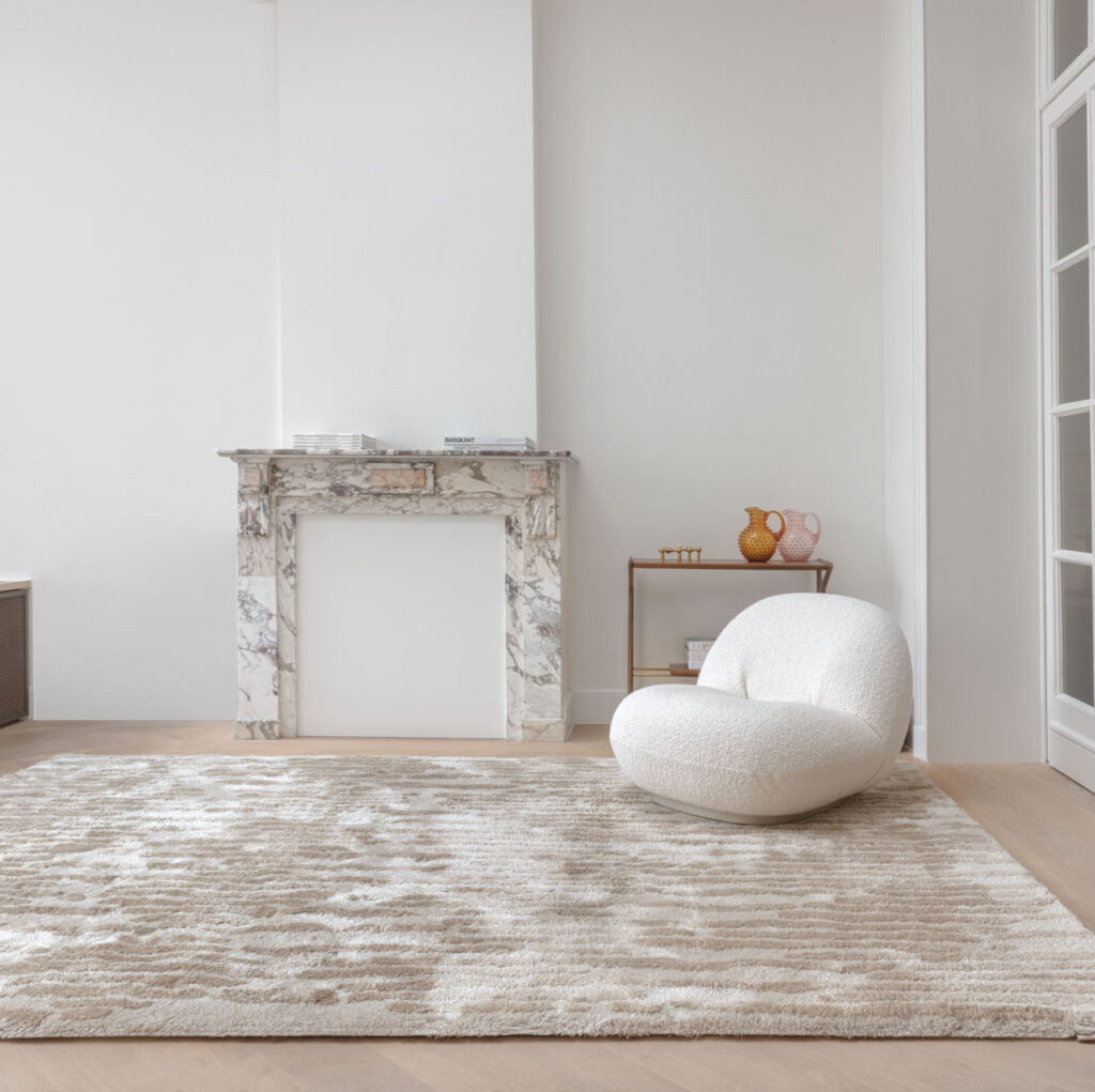 Modern interieur met het Limited Edition-vloerkleed Cosmic Vista in de kleur White Pepper voor een marmeren haard en witte designfauteuil.