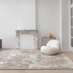 Modern interieur met het Limited Edition-vloerkleed Cosmic Vista in de kleur White Pepper voor een marmeren haard en witte designfauteuil.