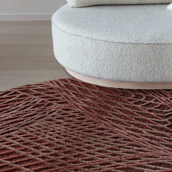Rond vloerkleed Spiro in auburn bruin met een reliëfpatroon, geplaatst voor een ronde, lichtkleurige bank.