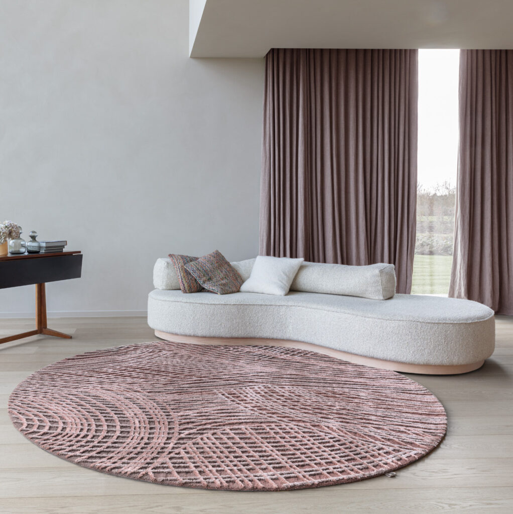Ronde Limited Edition Spiro BrushPink vloerkleed in een moderne woonkamer met lichtgebogen witte sofa en roze gordijnen.
