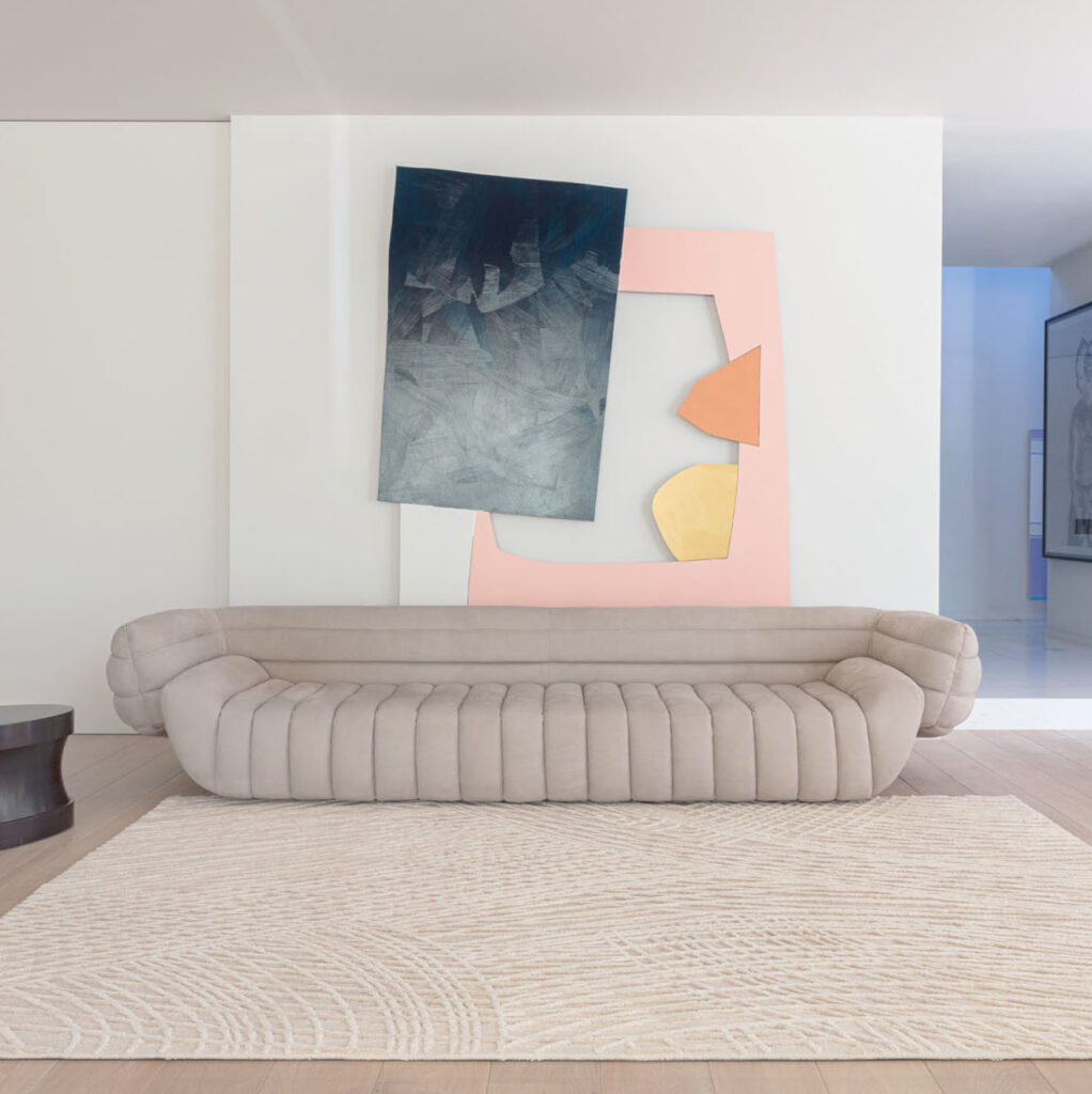 Beige Limited Edition vloerkleed Spiro Summer Sandoh voor een moderne, lichtgrijze designbank met abstracte kunst aan de muur.