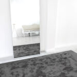 Donkergrijs limited-edition vloerkleed Astral Gunmetal in een minimalistisch ingerichte kamer met spiegel en klassieke bank.