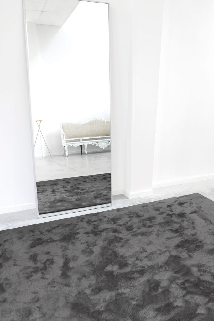 Donkergrijs limited-edition vloerkleed Astral Gunmetal in een minimalistisch ingerichte kamer met spiegel en klassieke bank.